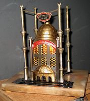 Front view showing brass-colored mosque structure with dome, minarets, and light perforations mounted on marble base.