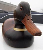 Close-up image showing the front and upper body detail of the carved wood mallard duck decoy with glass eyes and natural wood finish.