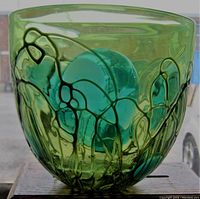 Front view of greenish-turquoise blown glass vase showing pulled feather design pattern with raised lines and bubbles inside glass.