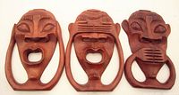 Full view of three teak wood carved wall heads, life-size, representing hear no evil motif