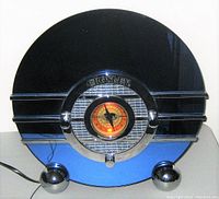 Front view of vintage Crosley radio cassette player showing cobalt blue circular glass panel with chrome horizontal bars, illuminated dial and spherical feet.