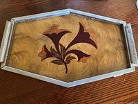 Top view of Art Deco serving tray showing the veneer wood grain and lily pattern, metal edging and handle.