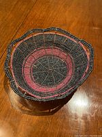 Photo of a handmade decorative bowl crafted from small glass beads in black, pink, and white hues, arranged in concentric circles on a wire frame with a scalloped edge.