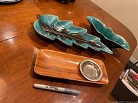 Two ceramic leaf-shaped serving dishes on a wooden table alongside a rectangular teak serving dish with a metal inset dish. A marker pen included for size reference.