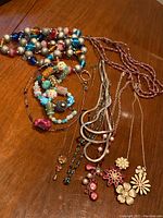 Overhead photo showing mixed costume jewellery laid out on wood surface, including necklaces and bracelets with beads, charms and floral pendants.