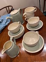 Teapot, milk jug, six tea cups and six saucers displayed on wooden table, showing full set with Energy pattern and cream interiors.