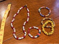 Photo of handmade glass bead necklace and four bracelets laid out on wooden surface with a measuring tape showing necklace length.