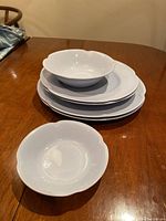 Set of white ceramic Johnson Brothers Greydawn dishes, plates and bowls, shown stacked on a wooden table.