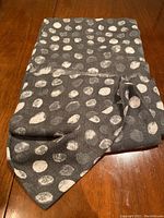 Folded gray shawl or scarf showing white circular patterns and texture on wood surface