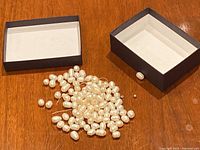 Loose pearls spilled from a small open jewelry box on a wooden surface, showing multiple white cream-colored pearls with irregular shapes and sizes.