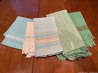 Five handwoven linens displayed on a wood surface arranged horizontally showing color and pattern detail
