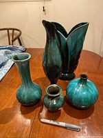 Five blue mountain vases and jug on wooden table, showing large tulip vase signed and smaller vases with blue-green glaze finish.