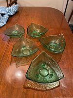 Top-down view of five green glass triangular candlestick holders arranged on a wood table.