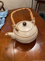 Full view of mid-century modern ceramic teapot sitting on wooden table, showing bamboo handle and spout.