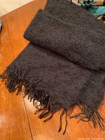 Photo of folded black mohair shawl laid on wooden surface, showing texture and fringed ends