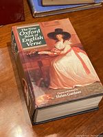 Front cover of 'The New Oxford Book of English Verse' showing dust jacket with woman in white dress and black hat seated at table.