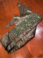 Silk belt in olive green color laid out on wooden surface, showing embroidered beadwork and fabric texture.