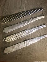 Four silk ties laid flat showing front design and patterns: plaid, dotted, geometric, solid color.