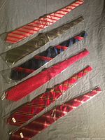 Six silk ties laid flat on a gray surface showing their full length and pattern details.