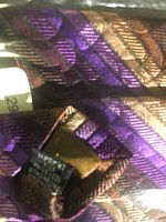 Close-up of fabric and pattern on purple and bronze silk tie with tags visible