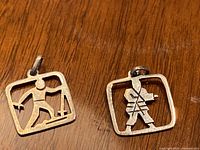 Two silver charms showing front side with figures inside square frames on wooden surface