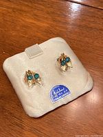 Top view showing pair of gold fill screw back earrings with blue stones and leaf design on original cream cushion holder.