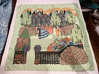 Full view of the scarf laid flat showing detailed garden scene with people and flowers on a pastel green background.