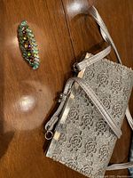 Photo showing vintage rhinestone brooch and silver floral clutch purse on a wood surface.