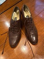 Pair of dark brown leather lace-up women's shoes with pointed toes and stacked heels on wooden surface.