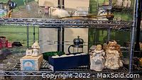 Wide shot showing two porcelain dolls, a decorative box shaped like a house, and various glass and ceramic items on metal wire shelving.