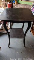 Top-down angled view of antique black lacquer wooden table showing curved legs and lower shelf, surface wear visible