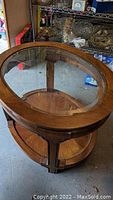 Clear detailed view of the round glass top embedded in wood frame with visible wood grain and lower shelf.