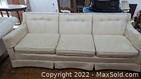 Off-white three-seat couch front view showing seat cushions and button tufting on back cushions. Couch fabric appears lightly stained and used.