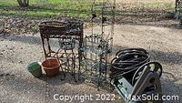 Overview of metal and wooden plant stands, plastic pots, and garden hose on reel laid out on concrete patio.