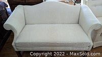 Small off-white vintage couch from front view showing rolled arms, cushioned seat and patterned upholstery.