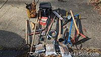 Photo shows collection of various vintage and gardening tools spread on the ground including an electric vibrating sander, hand tools, pruning shears, rakes, shovels, and wire coil.