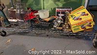 Photo of a metal wire shelf holding vintage roller skates, silver plated candle sticks, meat grinders, glass jug, boxed wooden toy cars, and other kitchen and household items.