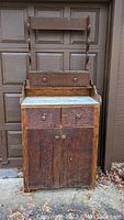 Front view of antique wooden workbench showing upper rack, two drawers, cabinet doors, and worn surface