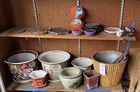 Full display of various Asian style garden pots, planters, decorative lanterns, candleholders, and other items on wooden shelves against pegboard.