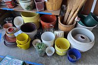 Full arrangement of multiple garden pots of clay, ceramic, metal, and glass materials alongside wooden containers and yellow and blue pots, plus small glass jars and planters.