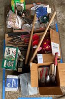Photo showing multiple gardening hand tools including pruning shears, scissors, hand shovels, garden tape, gloves, and boxed garden chemicals and supplies.