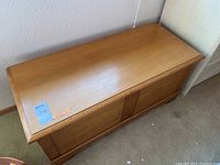 Top view of cedar chest showing rectangular wooden lid surface with seller labels for lot number and dimensions.