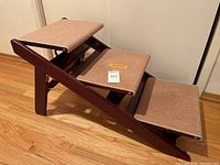 Side angled view of 3-step pet stairs showing each step carpeted in tan and sturdy dark wood frame, collapsed into stair form.