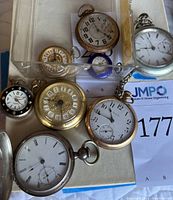 Overhead view of assorted pocket watches in plastic tray showing varied sizes and metal finishes
