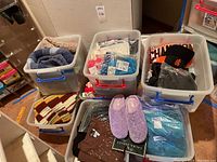 Overview of eight plastic tubs filled with assorted clothing items.