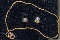 Pair of gold stud earrings with round white stones and gold chain bracelet displayed on black background