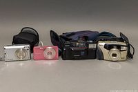 All four cameras and three carrying cases arranged in single row on neutral surface.