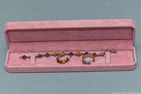 Full view of bracelet and earrings in a pink velvet-lined box, bracelet is approximately 7 inches long with various shaped amber stones in silver settings.