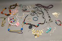 Top-down view of assorted costume necklaces, bracelets, bangles spread out on neutral grey background showing variety and colors.