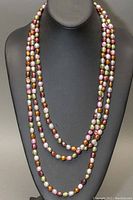 Front view of the long multistrand lariat necklace showing vibrant multicoloured dyed baroque pearls on black display bust.